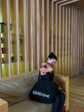 Woman holding a black bag with 'Mardoshe' branding in a room with wooden walls and shelves.
