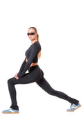 Woman in black athletic wear stretching on a white background